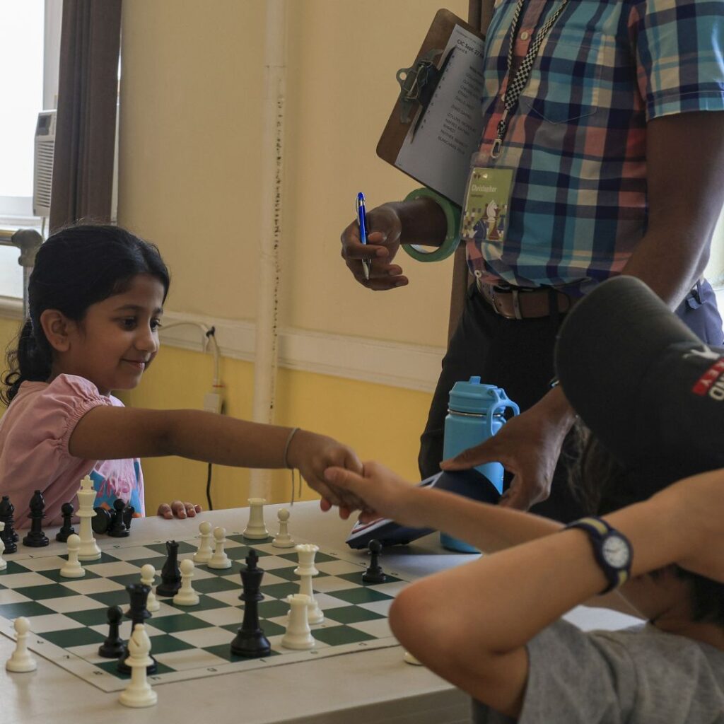 Girl shakes hands with opponent at chess match.