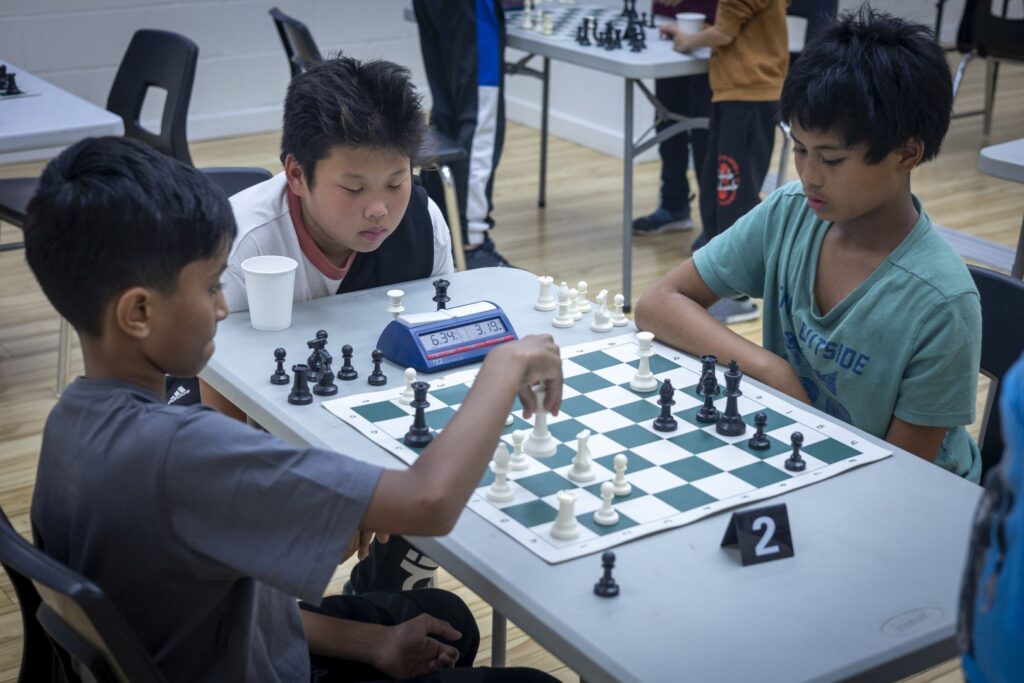 Boy looking on as two others play chess